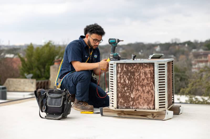 A Wright AC Services technician working on an outdoor HVAC unit on top of a building.