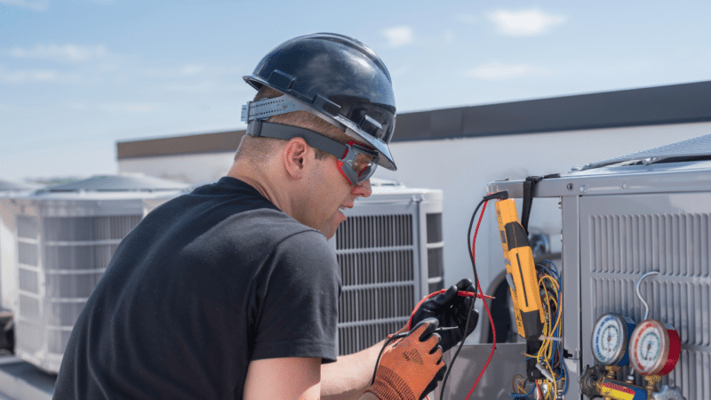 An HVAC technician working on an outside unit on top of a roof.