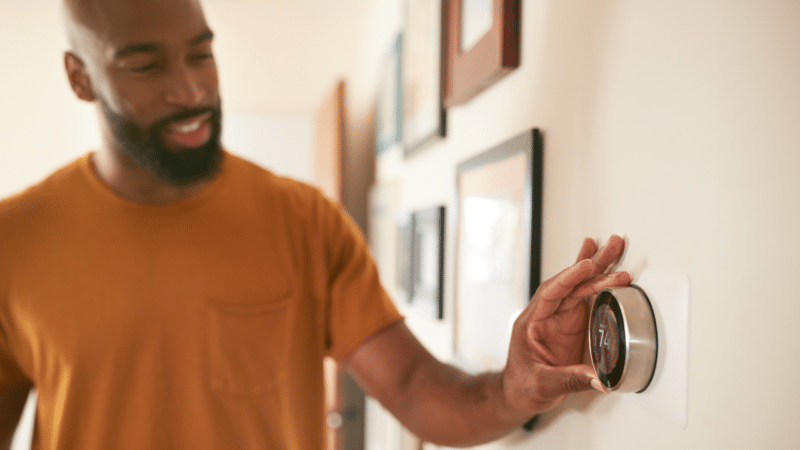 A man reaching for the thermostat on the wall to adjust the temperature.